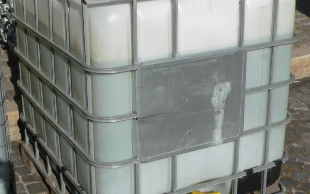 Caged plastic IBC tote on a wooden pallet with a red top fill cap and a yellow bottom discharge valve