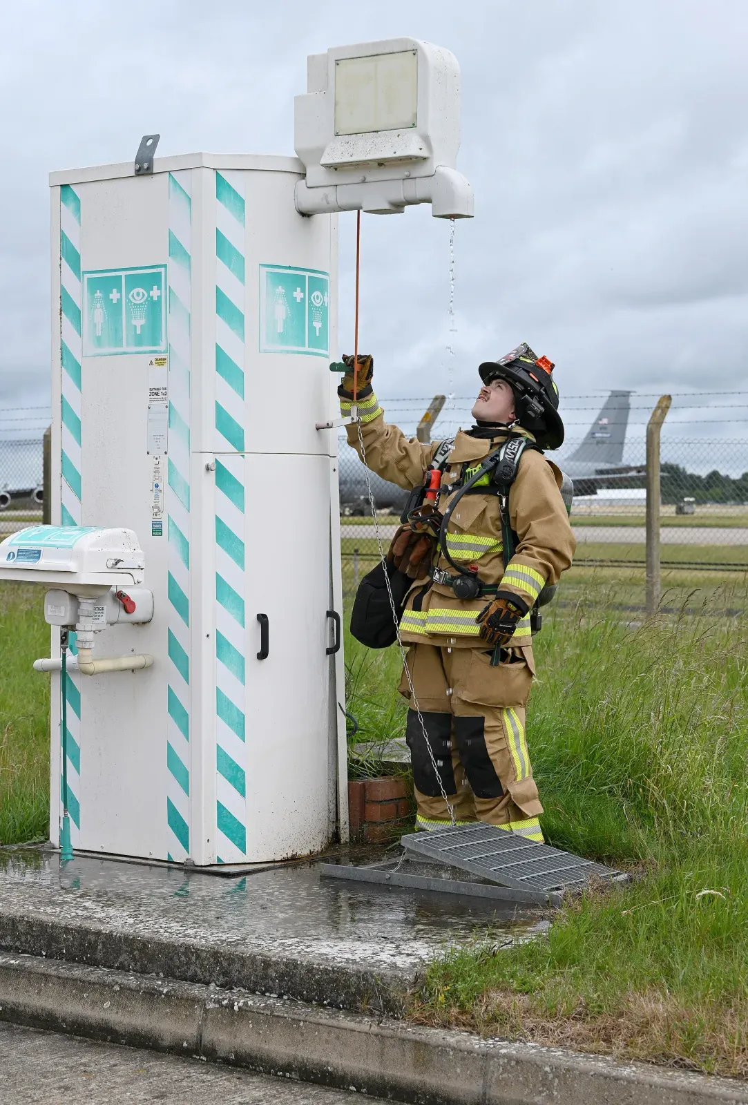 Firefighter in turnout gear pulling the activation rod on an outdoor emergency safety shower and eyewash combination unit during a fuel spill drill