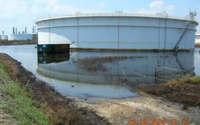 Large white storage tank standing in floodwater inside an overtopped containment berm