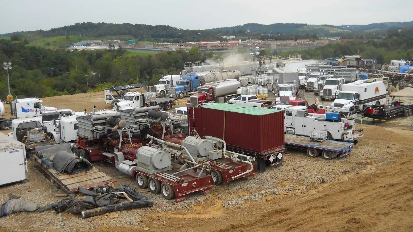 Hydraulic fracturing location crowded with pump trucks, iron and support vehicles on a gravel pad