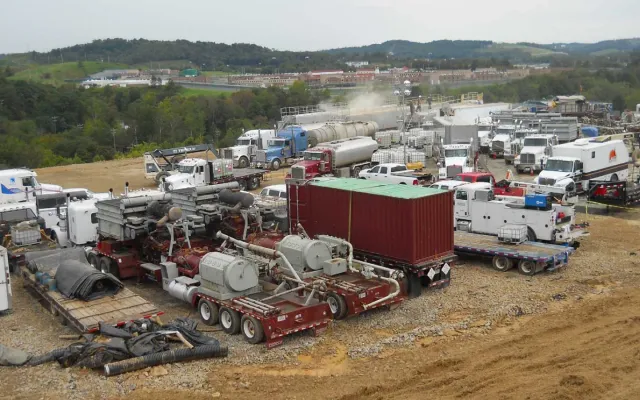 Hydraulic fracturing location crowded with pump trucks, iron and support vehicles on a gravel pad
