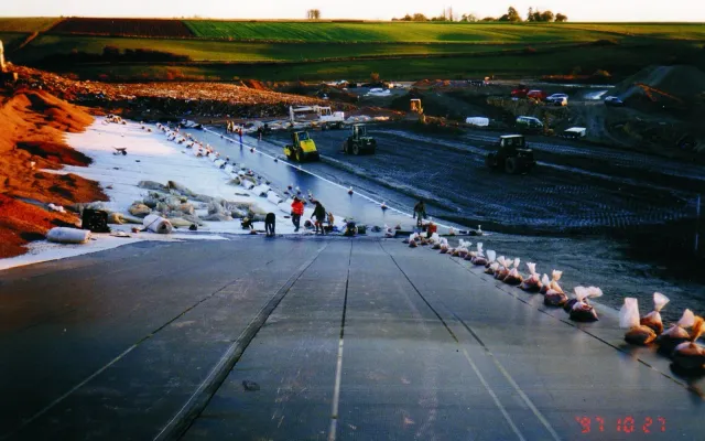 Crew installing black geomembrane liner panels across a large graded slope