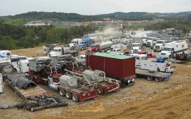 Hydraulic fracturing well site with pump trucks, frac iron, tanks and support trucks spread across a gravel pad