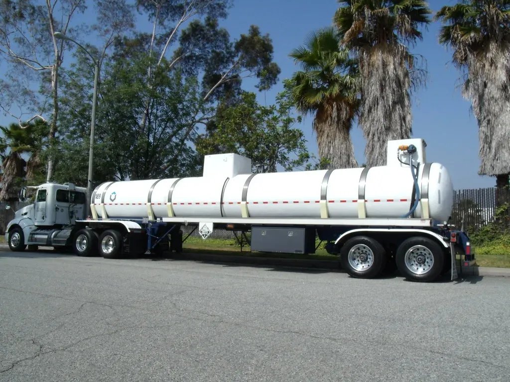 Stainless tank trailer behind a truck tractor, the kind of oil patch tanker that parks inside a drive-over containment berm to load or unload