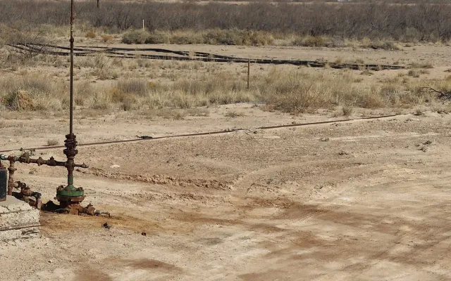 Wellhead and surface flowline on bare caliche at a pumpjack near Monahans, Texas, where a leak would become oil contaminated soil