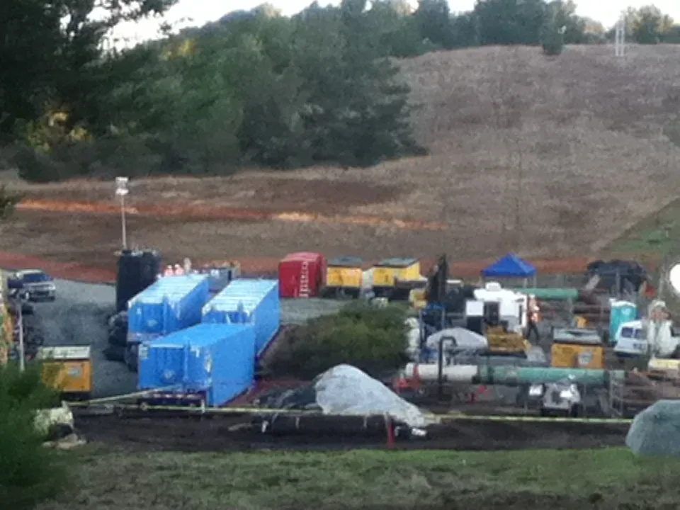 Pipeline hydrostatic test spread at the pressurization point, with blue water tanks, test equipment and a section of pipe behind a barricade tape line
