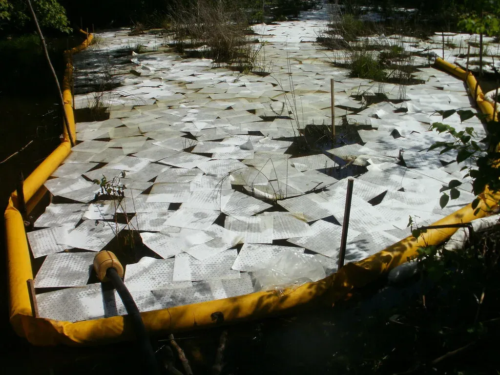 Hundreds of white absorbent pads laid on spilled diesel inside a yellow containment boom, showing how many pads a modest spill takes