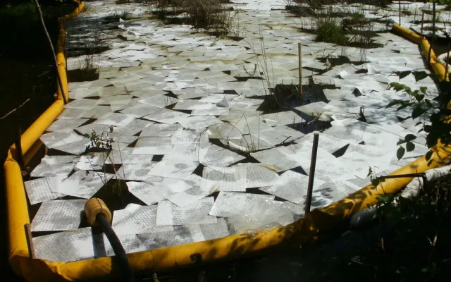 Hundreds of white absorbent pads laid on spilled diesel inside a yellow containment boom, showing how many pads a modest spill takes