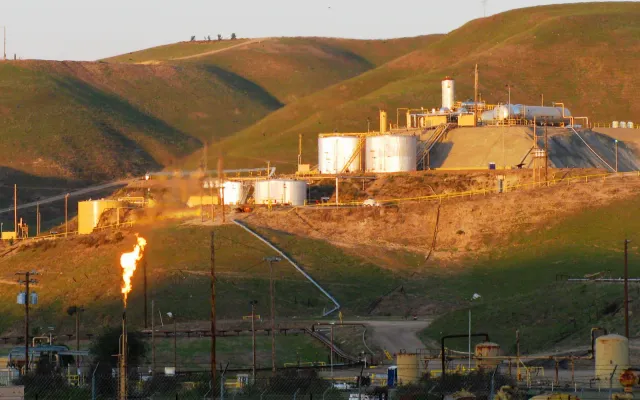 Oil field tank battery with storage tanks, pipe racks and a gas flare on a hillside, the kind of production site an SPCC inspection covers