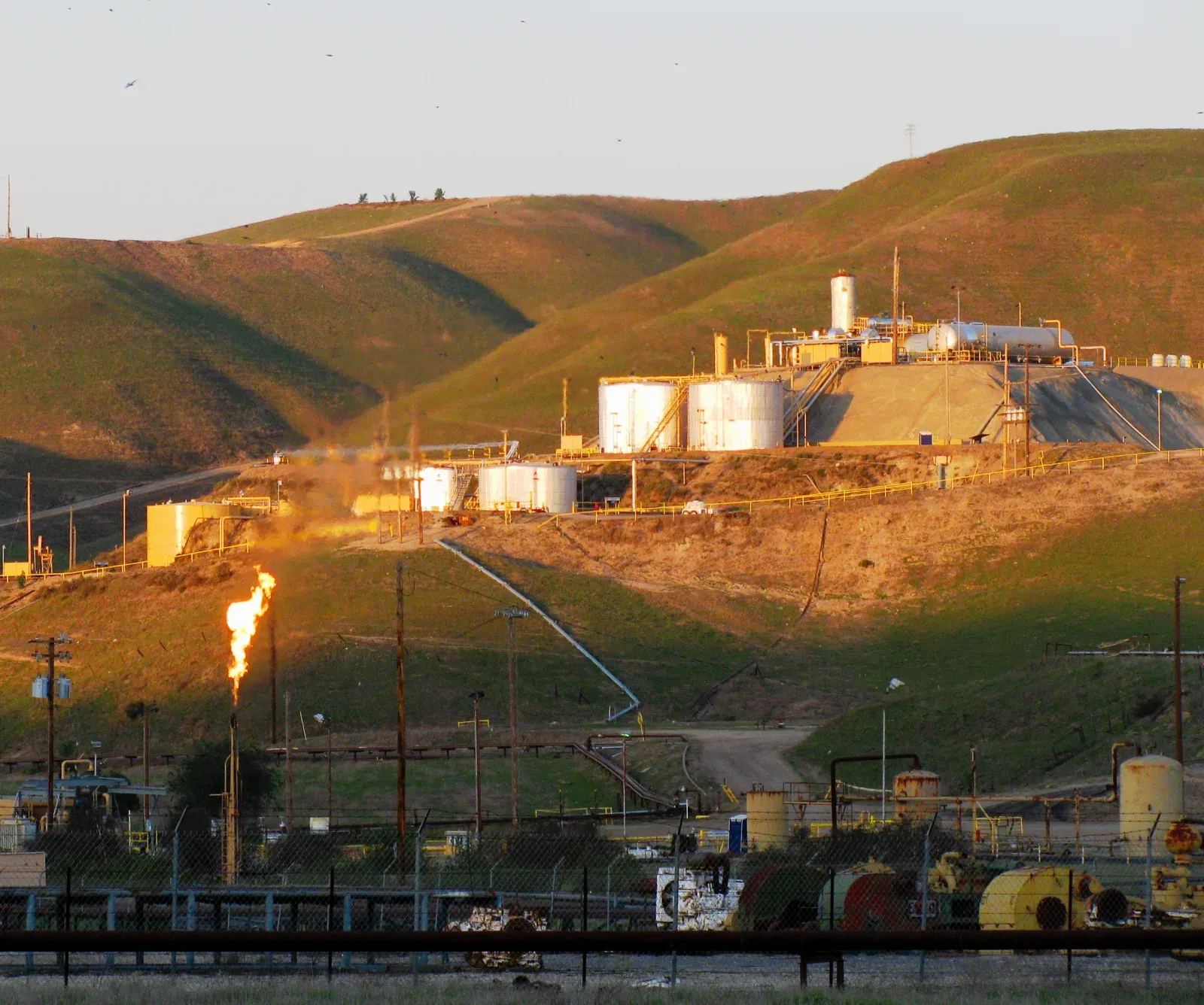 Oil field tank battery with storage tanks, pipe racks and a gas flare on a hillside, the kind of production site an SPCC inspection covers