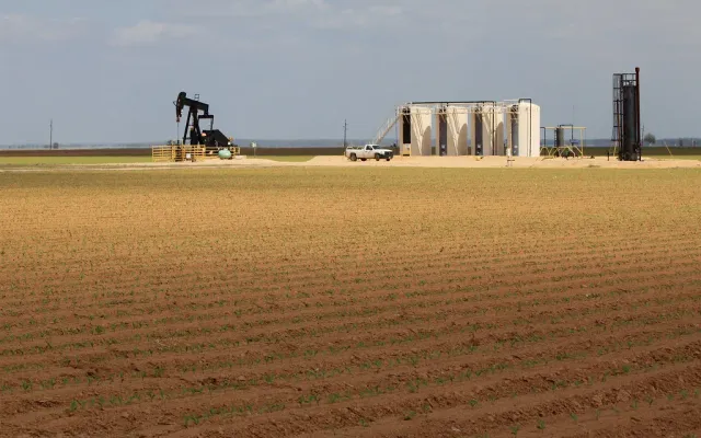 Oil well tank battery with vertical steel tanks and a pumpjack on a lease in Texas, the kind of site that needs secondary spill containment
