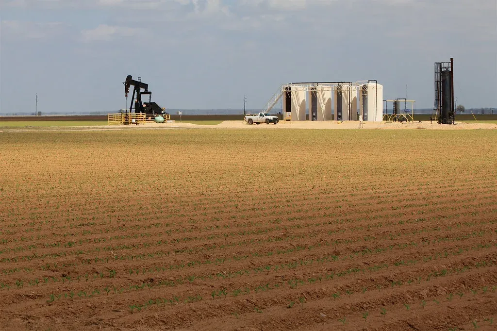 Oil well tank battery with vertical steel tanks and a pumpjack on a lease in Texas, the kind of site that needs secondary spill containment