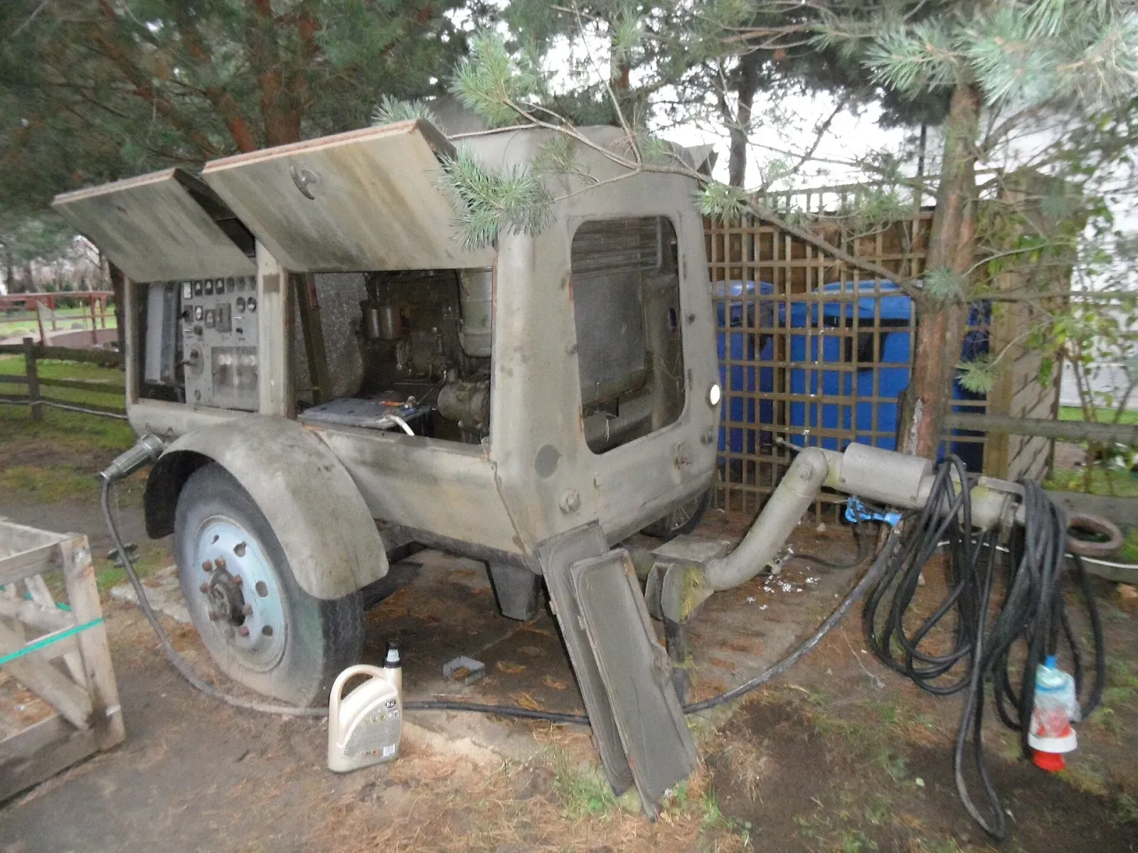 Trailer-mounted diesel generator with its panels open, parked on bare ground with an oil jug and cables beside it and no spill containment underneath
