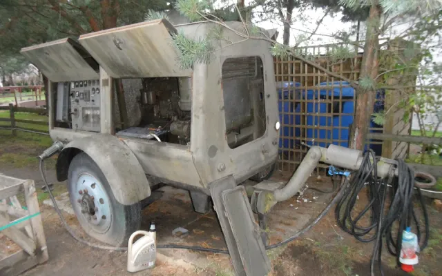 Trailer-mounted diesel generator with its panels open, parked on bare ground with an oil jug and cables beside it and no spill containment underneath