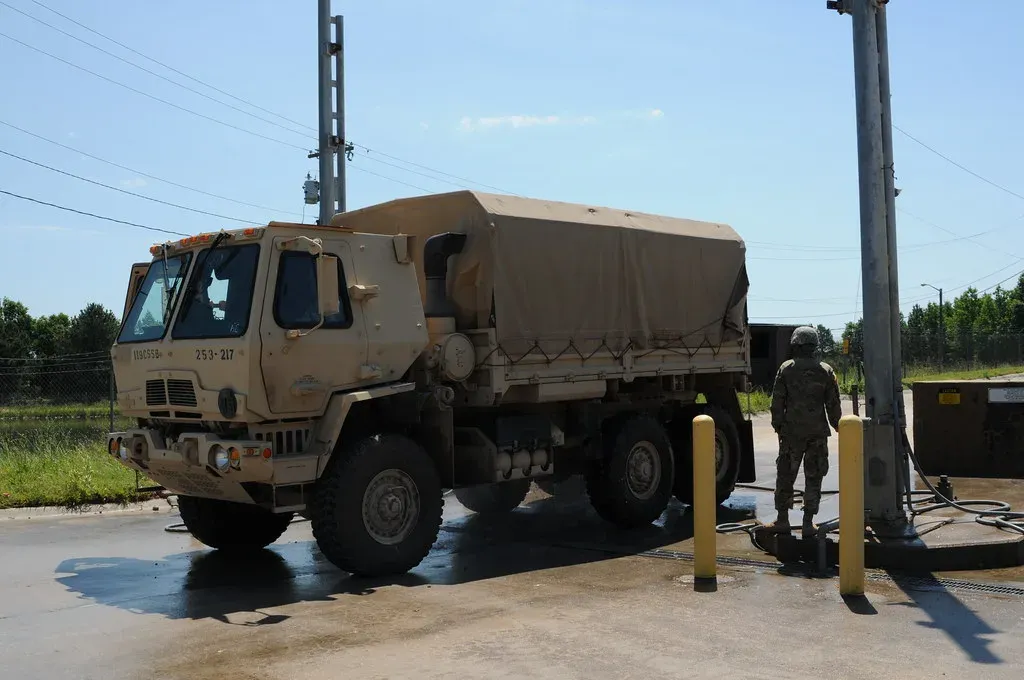 Military cargo truck parked on a concrete wash rack with a hose station and bollards, an example of a fixed wash pad with drainage