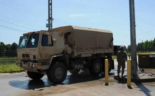 Military cargo truck parked on a concrete wash rack with a hose station and bollards, an example of a fixed wash pad with drainage