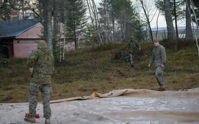 Two workers with a hose washing a tan spill containment berm liner laid out on the ground