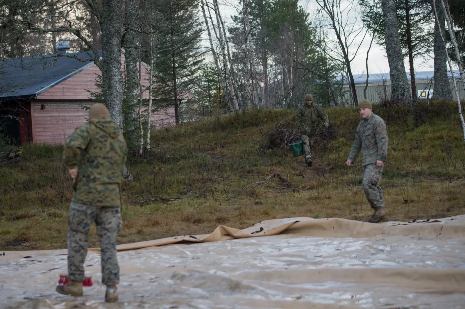 Two workers with a hose washing a tan spill containment berm liner laid out on the ground