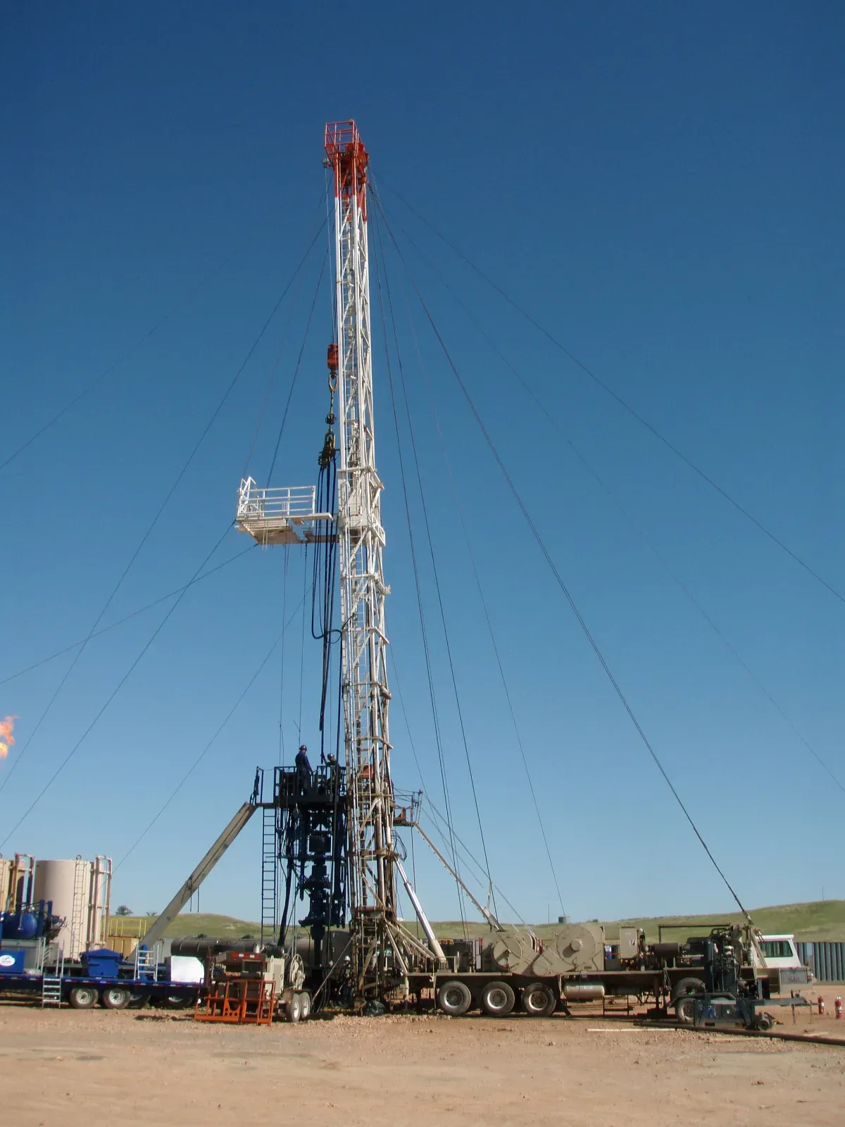 Truck-mounted workover rig with its mast raised over a wellhead and BOP stack during a snubbing job, with tanks and a flare in the background