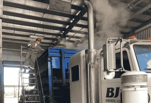 Worker steam cleaning a truck-mounted unit in a wash bay